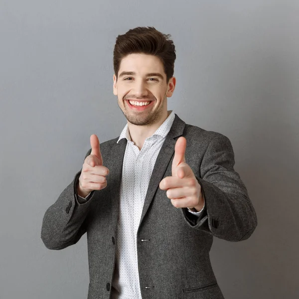 Portrait d'un homme d'affaires souriant en costume pointant la caméra contre un mur gris — Photo de stock