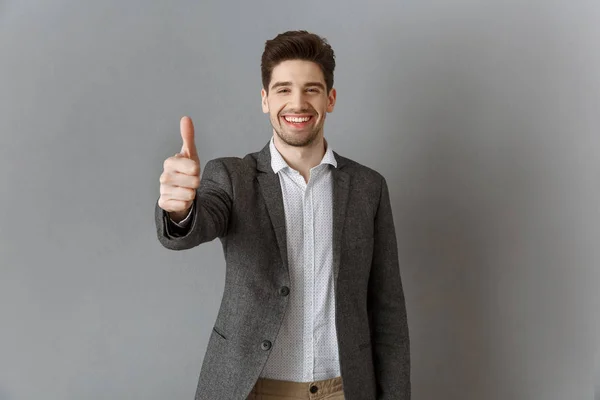 Portrait of smiling businessman in suit showing thumb up against grey wall — Stock Photo