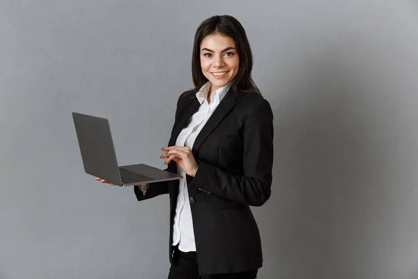 Vista lateral de mujer de negocios sonriente con portátil contra fondo de pared gris - foto de stock