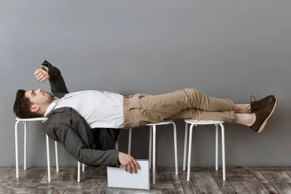 Empresário cansado com documentos verificando o tempo enquanto deitado em cadeiras e à espera de entrevista de emprego — Fotografia de Stock
