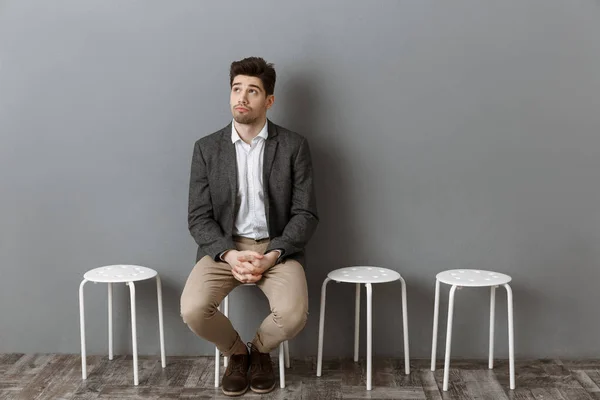 Cher homme d'affaires en attente d'un entretien d'embauche sur chaise contre mur gris — Photo de stock