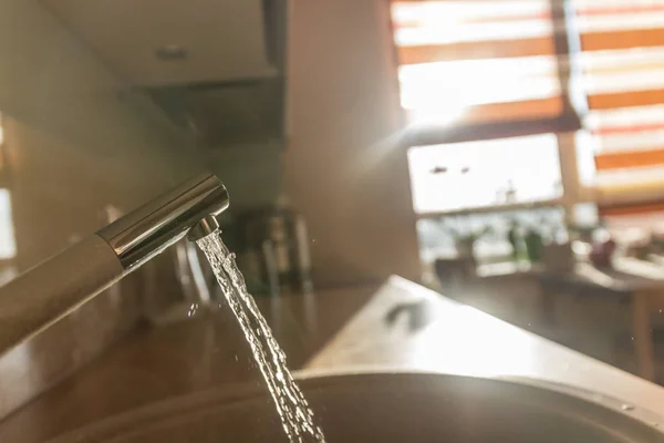 A stream of water pours from the tap in the morning on a blurred