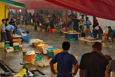 Sandakan. Malezya. 27 Kasım 2018. Deniz rıhtımındaki balık pazarı. Satıcılar ve alıcılar şemsiye ve tepe örtüsü altında sağanak yağmurun altında bekliyorlar.