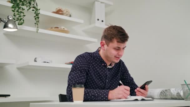 Молодой человек пишет и использует телефон в помещении . — стоковое видео