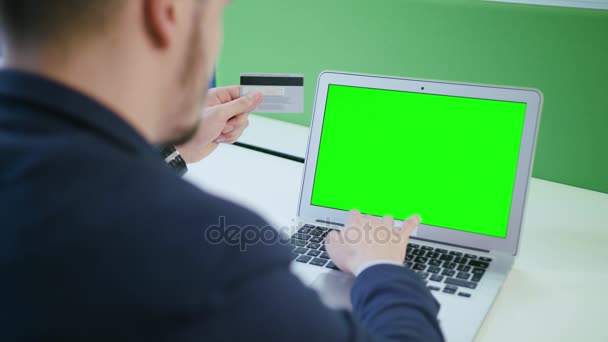 Un joven usando un ordenador portátil con una pantalla verde — Vídeo de stock