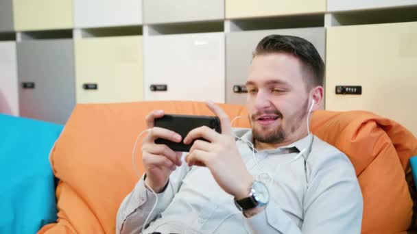 Мужчина играет в игры на смартфоне в помещении — стоковое видео