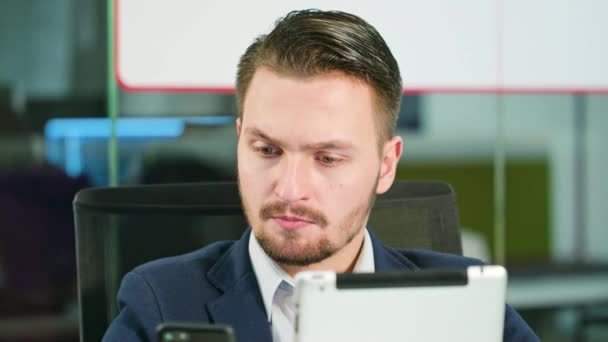 Joven usando un teléfono y una tableta en la oficina — Vídeos de Stock