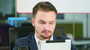 Ofiste bir telefon ve bir Tablet kullanan genç adam