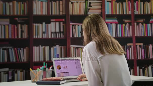 Joven dama usando un ordenador portátil en la biblioteca — Vídeos de Stock