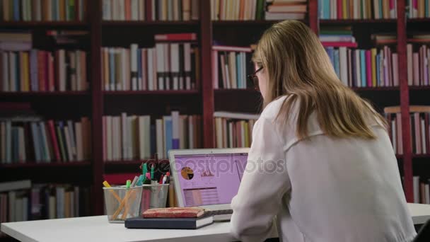 Jonge dame met behulp van een Laptop in de bibliotheek — Stockvideo