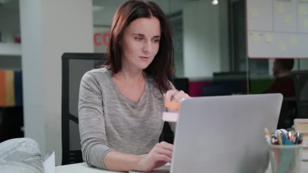 Дама сидить в офісі працює на ноутбуці — стокове відео
