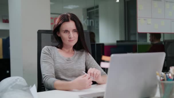 Женщина, сидящая в офисе и работающая над ноутбуком — стоковое видео