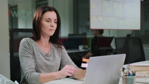 Женщина, сидящая в офисе и работающая над ноутбуком — стоковое видео