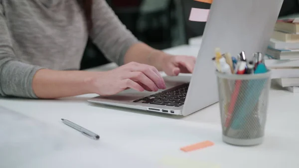 Женщина, сидящая в офисе и печатающая на ноутбуке — стоковое фото