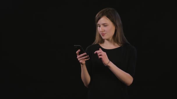 Een dame met behulp van een telefoon tegen een zwarte achtergrond — Stockvideo