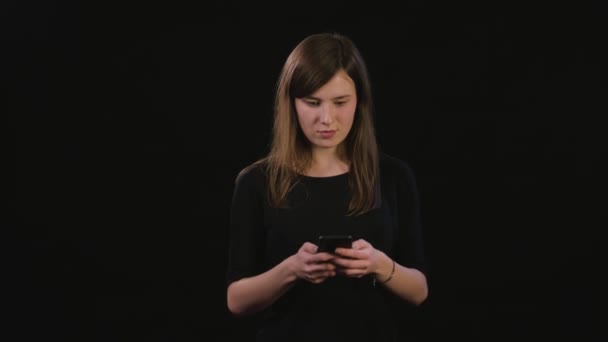 En dam med en telefon mot en svart bakgrund — Stockvideo