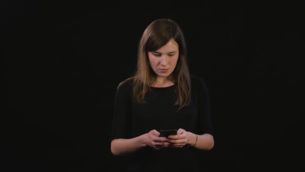 Een dame met behulp van een telefoon tegen een zwarte achtergrond — Stockvideo