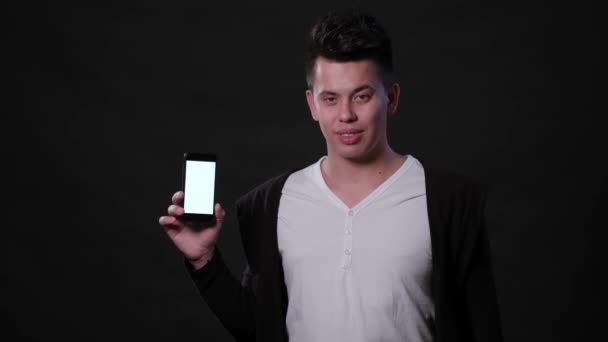 Un hombre sosteniendo un teléfono contra un fondo negro — Vídeos de Stock