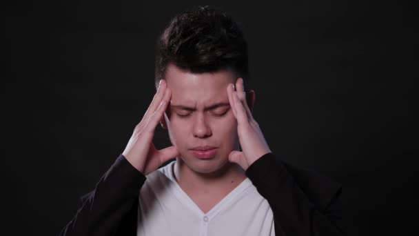 Un hombre que imita el dolor de cabeza contra un fondo negro — Vídeo de stock