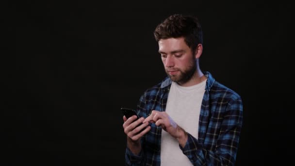Een Man met een telefoon tegen een zwarte achtergrond — Stockvideo