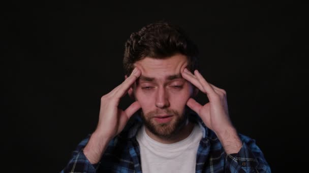Um homem imitando dor de cabeça contra um fundo preto — Vídeo de Stock