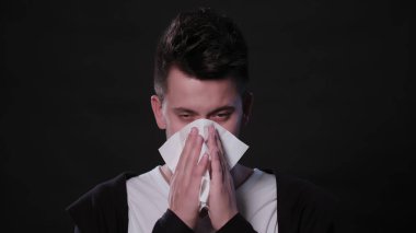 Bir adam siyah bir arka plan karşı onun burun üfleme