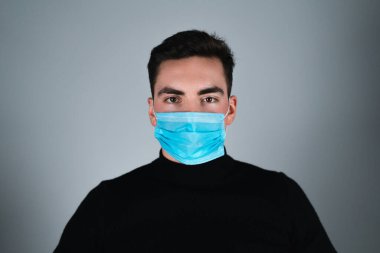 Siyah tişörtlü genç adam izole edilmiş gri arka planda tıbbi maske takıyor.