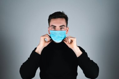Siyah tişörtlü genç adam izole edilmiş gri arka planda tıbbi maske takıyor.