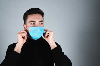 Siyah tişörtlü genç adam izole edilmiş gri arka planda tıbbi maske takıyor.