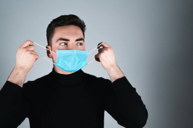 Siyah tişörtlü genç adam izole edilmiş gri arka planda tıbbi maske takıyor.