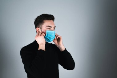 Siyah tişörtlü genç adam izole edilmiş gri arka planda tıbbi maske takıyor.