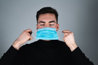 Siyah tişörtlü genç adam izole edilmiş gri arka planda tıbbi maske takıyor.