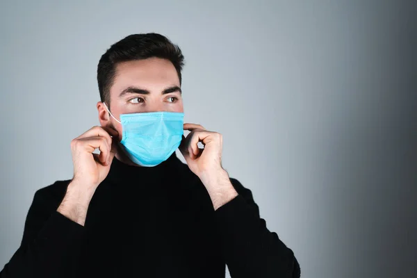 Siyah tişörtlü genç adam izole edilmiş gri arka planda tıbbi maske takıyor.