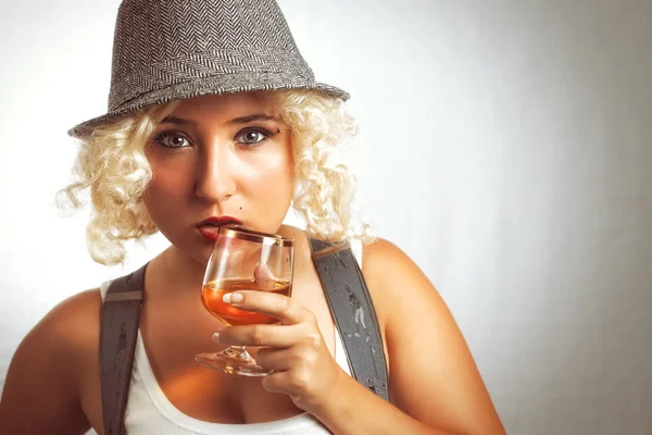 Knappe blonde vrouw in hoed, drinken van cognac. — Stockfoto