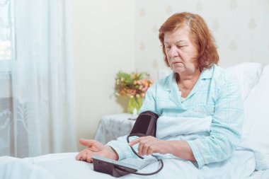Yaşlı kadın yatakta otururken ile dijital tansiyon aleti basınç ölçme.