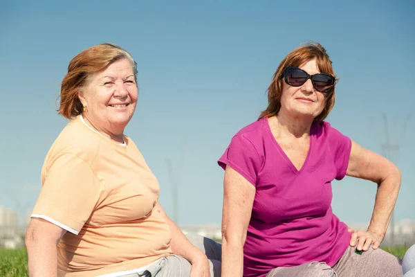 Dos mujeres mayores sentadas en el césped en el parque público . — Foto de Stock