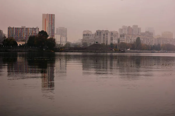 O rio no nevoeiro com o reflexo da cidade e o aterro — Fotografia de Stock