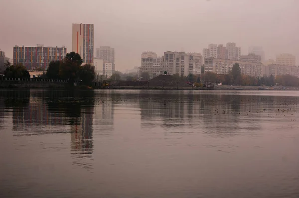 Der Fluss im Nebel mit dem Spiegelbild der Stadt und der Böschung — Stockfoto