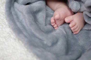 Yenidoğan bebek ayaklarını kapat. Küçük, tapılası pembe, pantolonlu, örgü elbiseli. Yatak çarşafında şirin bir bebek. Beyaz battaniyede yumuşak yün, üst tarafta. Mesaj için yer var. yumuşak odak.