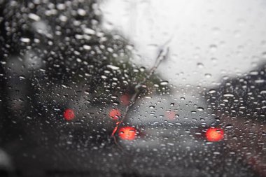 Akşam ları camın ön camına Yağmur Damlaları. şiddetli yağmurda sokak. Bokeh Kuyruk ışık ve trafik ışıkları şehirde. Lütfen arabayı dikkatli sür, kaygan yoldan. yumuşak odak.