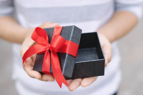 female hands holding open gift box dark black wrapped pack with beautiful red ribbon. for surprise special event with copy space. Christmas, birthday or new year concept. High resolution product.