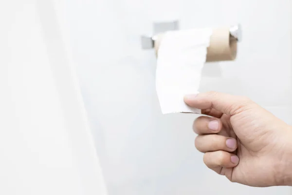 Hand pull Tissue Empty, Last pad out of toilet paper roll on white wall in public restroom.