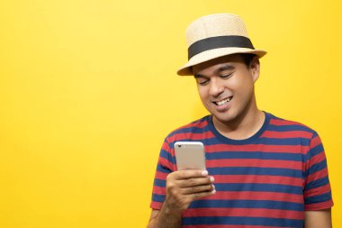 Sıradan giyinmiş neşeli Asyalı bir adamın portresi kırmızı çizgili tişört giyer ve gülümseyen bir şapka giyer ve kameraya başarı göstererek başparmağını kaldırır. sarı arkaplan üzerinde izole.