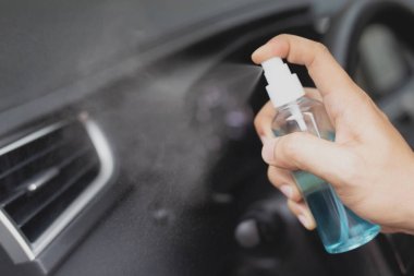 Adamın eli, arabasındaki direksiyona alkol püskürtüyor, dezenfektan püskürtüyor, Covid-19 virüsü enfeksiyonunu önlüyor, mikrop ya da bakteri bulaşmasını engelliyor, sık sık dokunulan temiz yüzeyleri siliyor.