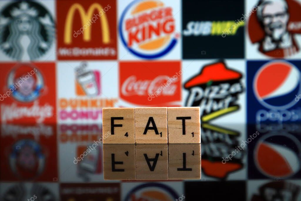 WROCLAW, POLAND - FEBRUARY 19, 2020: Word FAT made of wooden letters, and STARBUCKS, McDONALDS, BURGER KING, SUBWAY, KFC, WENDY'S, DUNKIN DONUTS, COCA COLA, PIZZA HUT, PEPSI logos in background