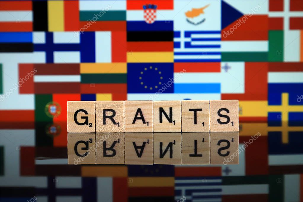 WROCLAW, POLAND - FEBRUARY 19, 2020: Word GRANTS made of wooden letters, and EUROPEAN UNION FLAG with flags of member countries in the background.