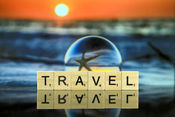 WROCLAW, POLAND - FEBRUARY 28, 2020: The word TRAVEL made of scrabble letters, sunset and view of a starfish through a glass, crystal ball (lensball) for refraction photography in the background.