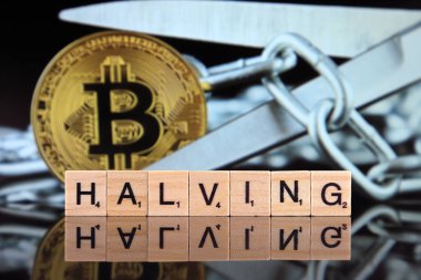 WROCLAW, POLAND - FEBRUARY 28, 2020: The word HALVING made of scrabble letters, physical version of Bitcoin and scissors in the background. Every 4 years the reward for adding a block is cut in half.