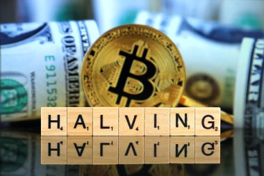 WROCLAW, POLAND - FEBRUARY 28, 2020: The word HALVING made of scrabble letters, physical version of Bitcoin and banknotes in the background. Every 4 years the reward for adding a block is cut in half.