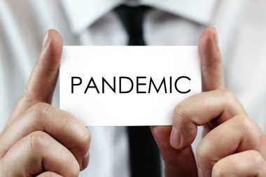 Beyaz gömlekli bir işadamı elinde PANDEMIC yazan bir kartvizit tutuyor. Coronavirus (COVID-19) küresel hastalık 2020.